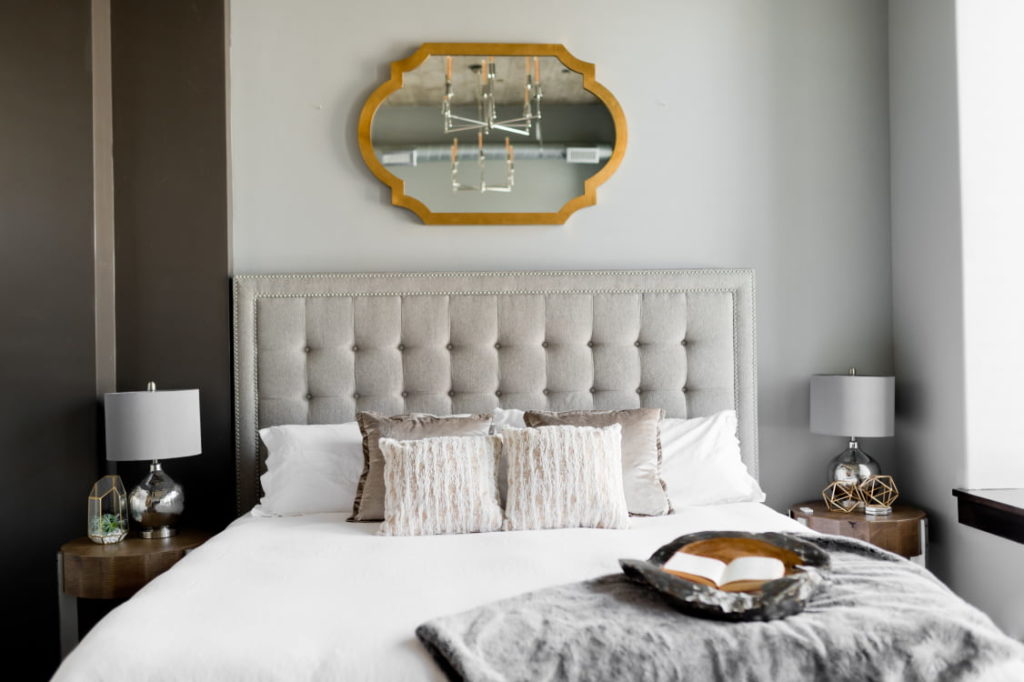 Photo of bed against a grey wall with grey headboard and white sheets