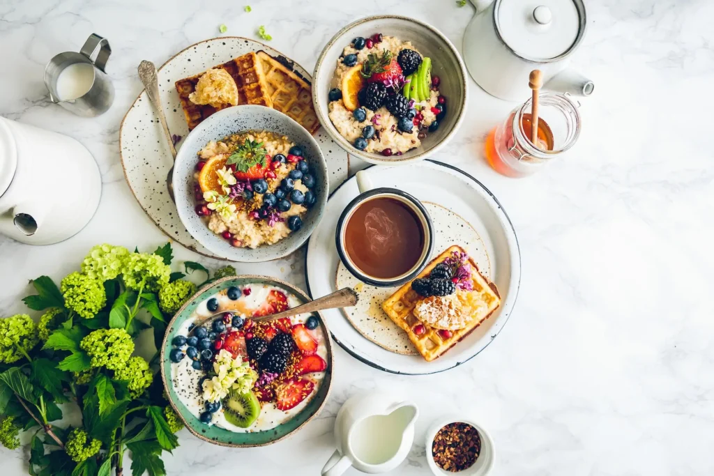 A brunch spread featuring bowls of oatmeal with fruit, waffles with butter and fruit, a cup of coffee and some sides