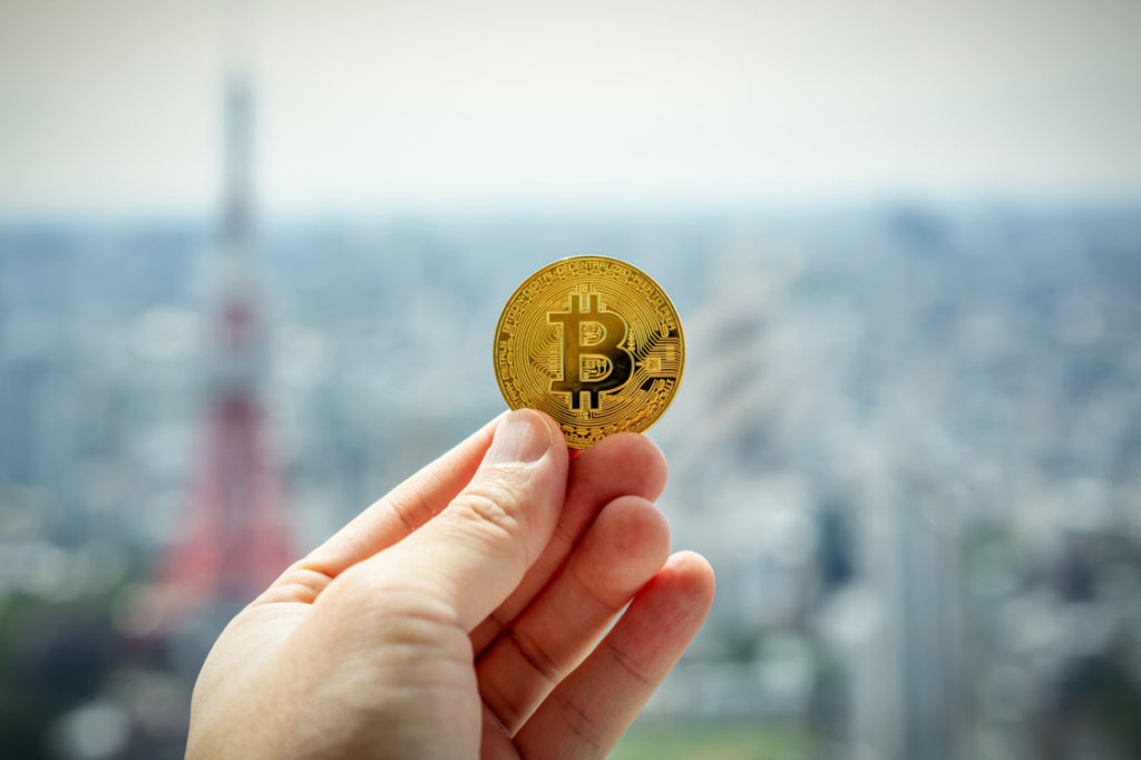 Hand holding fake Bitcoin coin against background of a blurry city