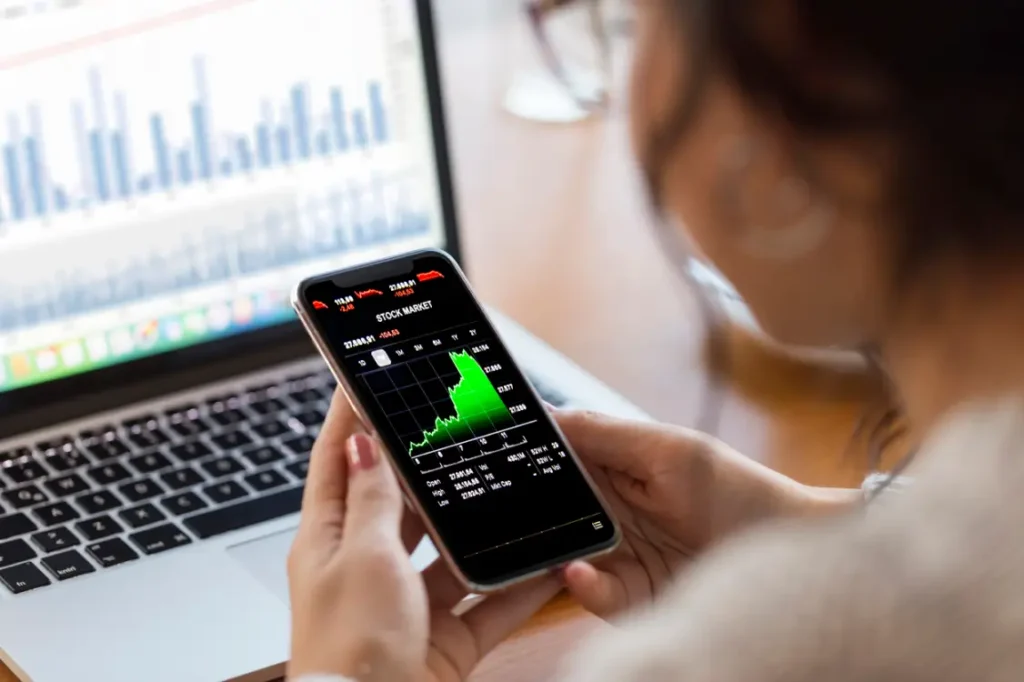 Woman looking at stock returns on her phone in front of a laptop