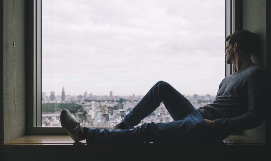 Person sitting alone in window sill looking out at city