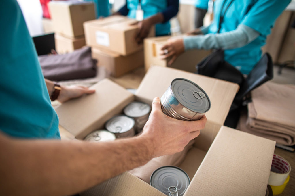 Hands of volunteers packing cans of food in boxes