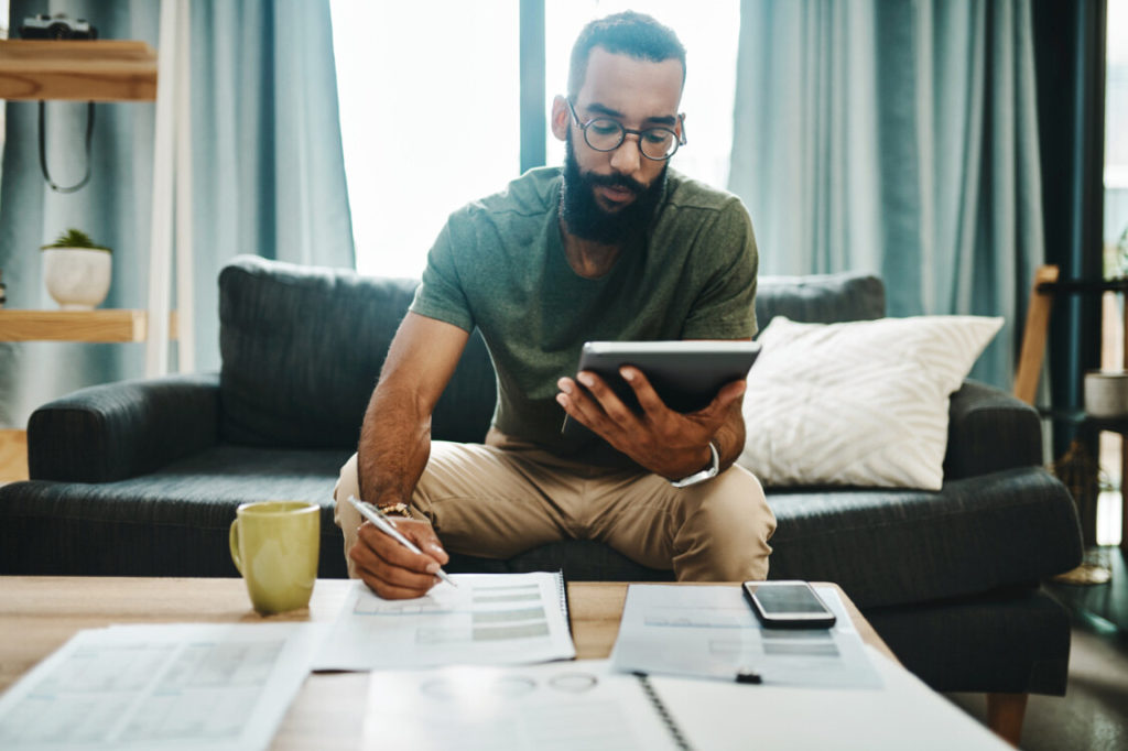 person reviewing documents on paper and tablet while sitting on sofa