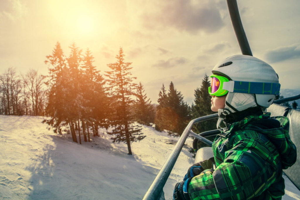 kid going up on ski lift look at snow covered mountain