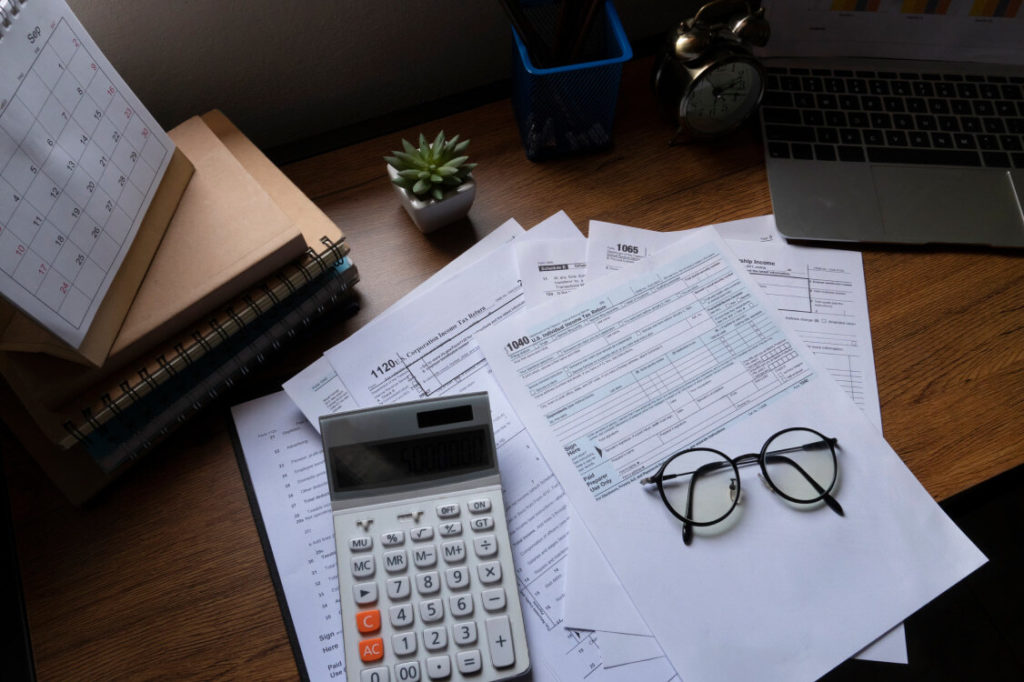 papers, calculator, laptop, glasses and portfolios resting on a desk