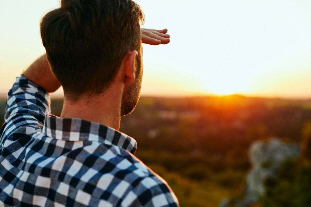 man looking at horizon blocking the sun as the sun sets