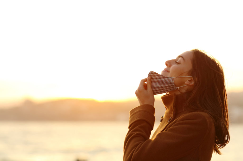 a woman removing her mask to take a breath of fresh air at sunset