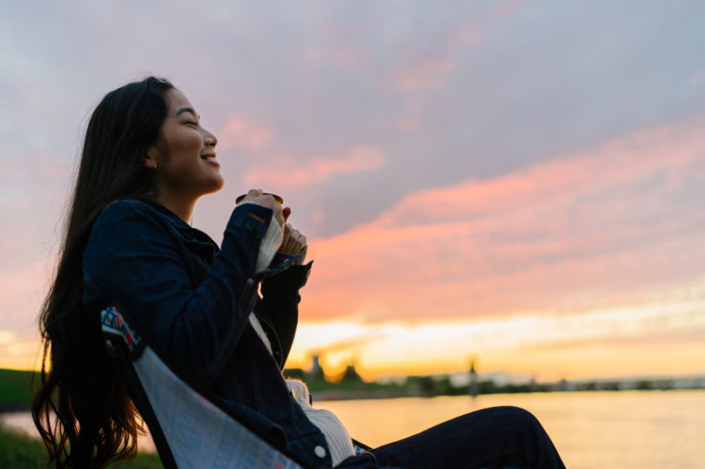 woman relaxing on the edge of a like with a mug in her hands