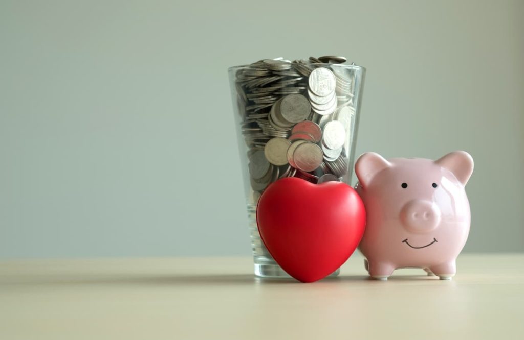 piggy bank next to a pint glass full of change with a read heart in front of it