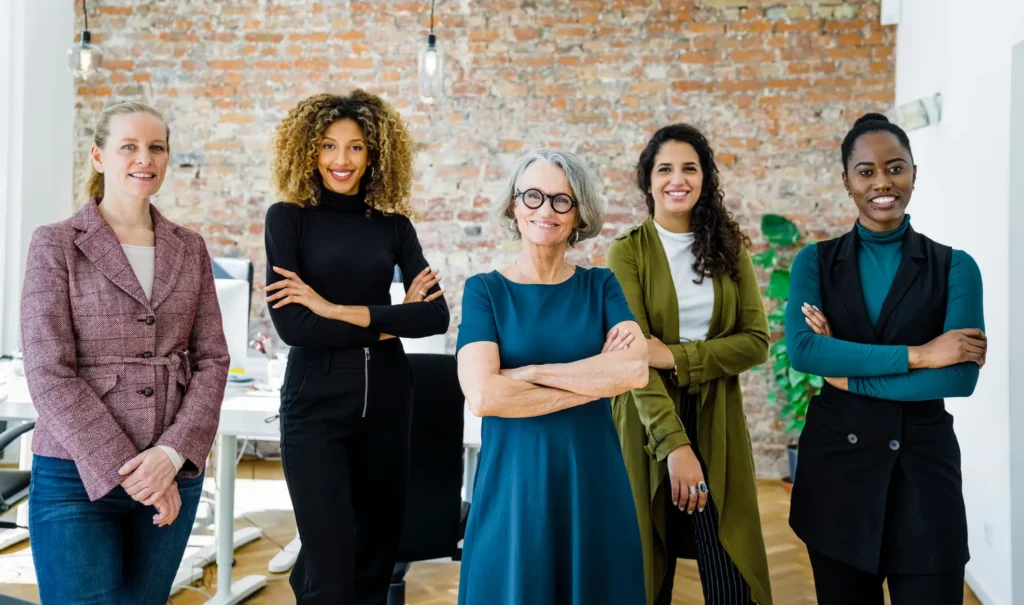 a diverse group of women standing against a brick wall with arms crossed