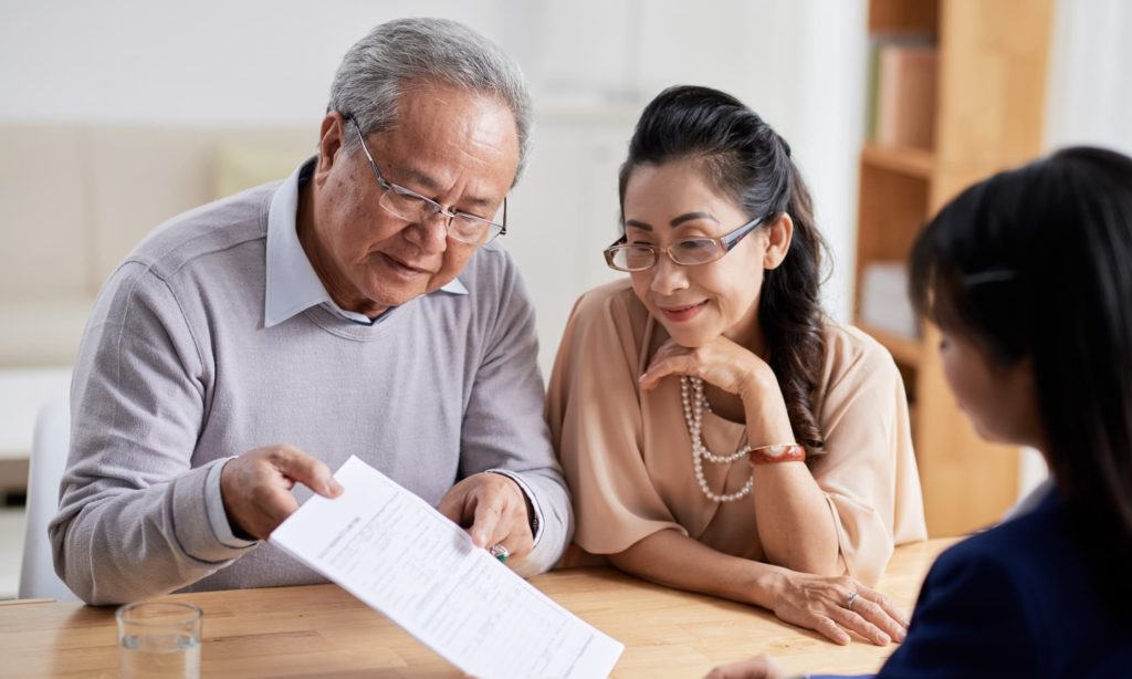 Senior husband and his wife studying financial document while having meeting with advisor, interior of modern office on background