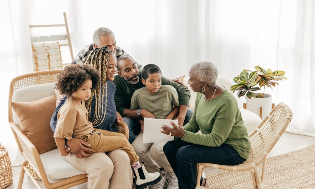 Family sitting in a living room while grandmother point to document