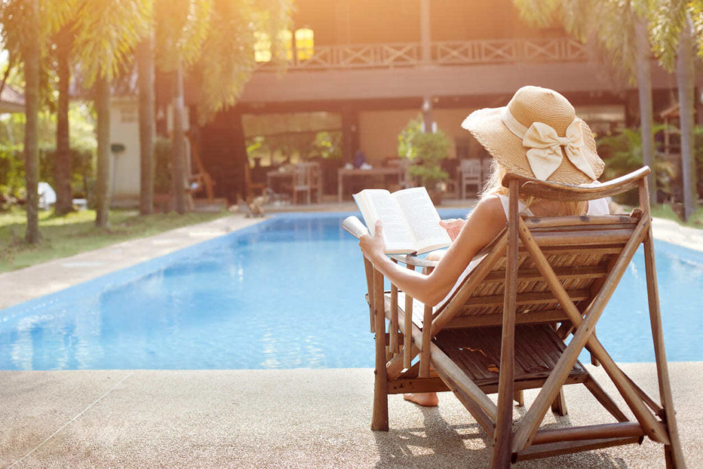 a woman wearing a hat reading a book near a pool