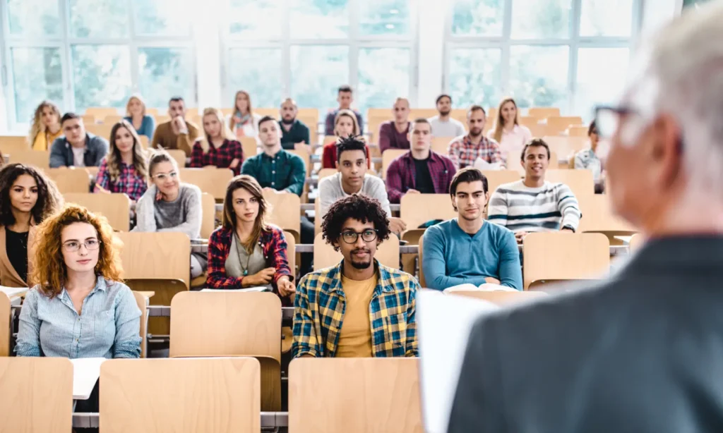 Panoramic view of large group of college students paying attention during a class in amphitheater.