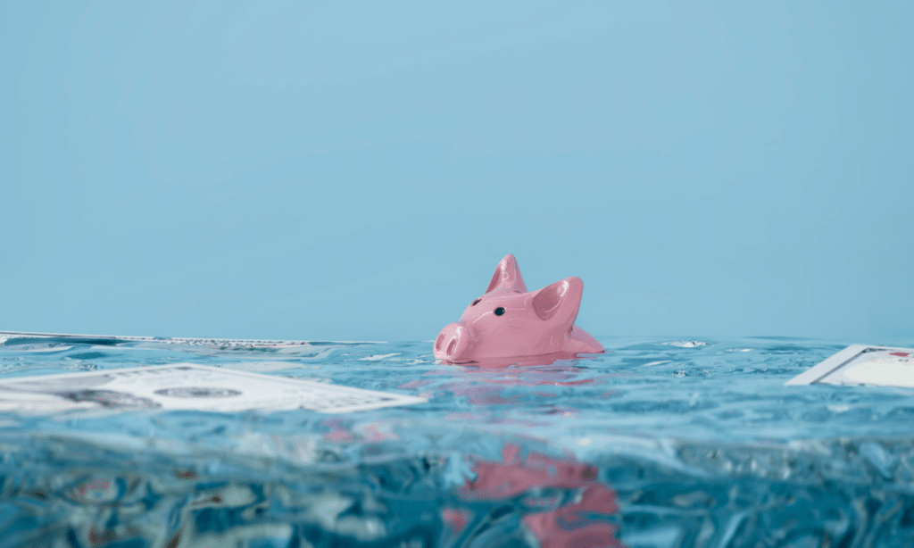 Bank collapse visualized as a piggy bank sinking underwater with 100 dollar bills in the water.