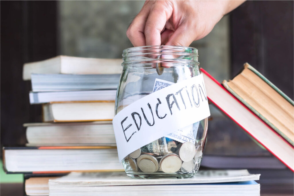 hand putting money to save for education. jar says education on it and is surrounded by books.