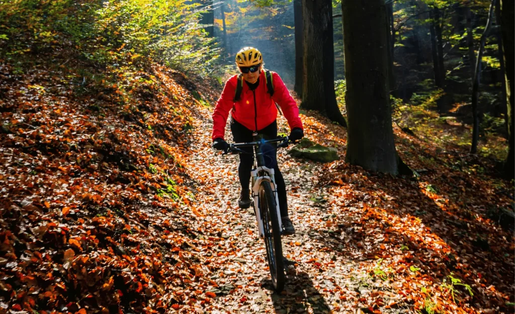 woman mountain biking in autumn. leaves fallen on the ground and she is riding in cold weather gear.