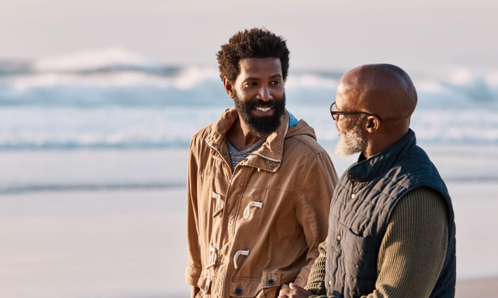 an older father and older son talking as they walk along a beach