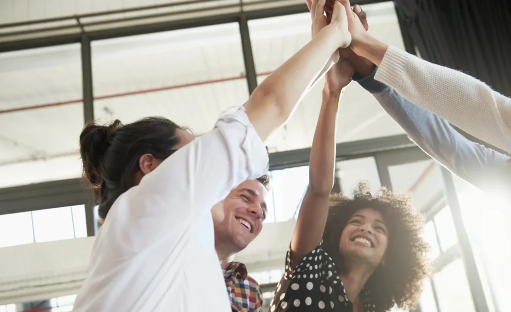 a team celebrating accomplishing their goals in an office setting with a group high five