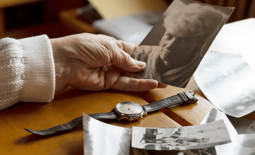 An old watch next to an old woman's hand. Next to old photos. Memories, nostalgia, time concept. Symbolizing a loved one has past.