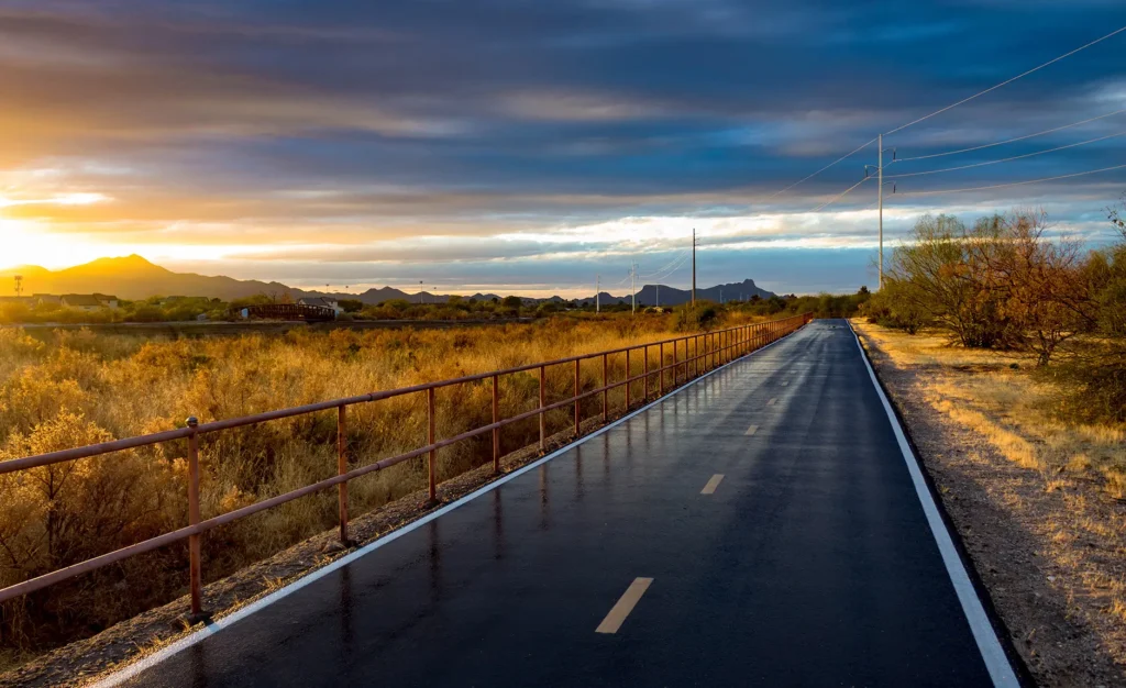 A portion of The Loop walking, biking, running and jogging path in Tucson, Arizona. A beautiful Sonoran Desert Sunset lights up the sky and the roadway wet with recent rain reflects the railing. 2018.