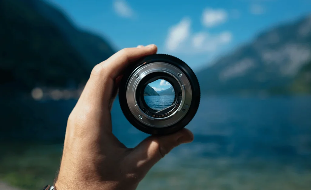 a photo of a hand holding a lens. the photo is out of focus except for the center of the lens. which focuses on an alpine lake.