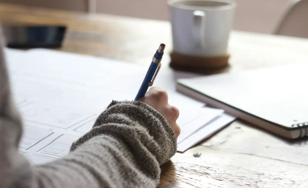 seated woman taking hand written notes in a notebook on a table in a coffee shop