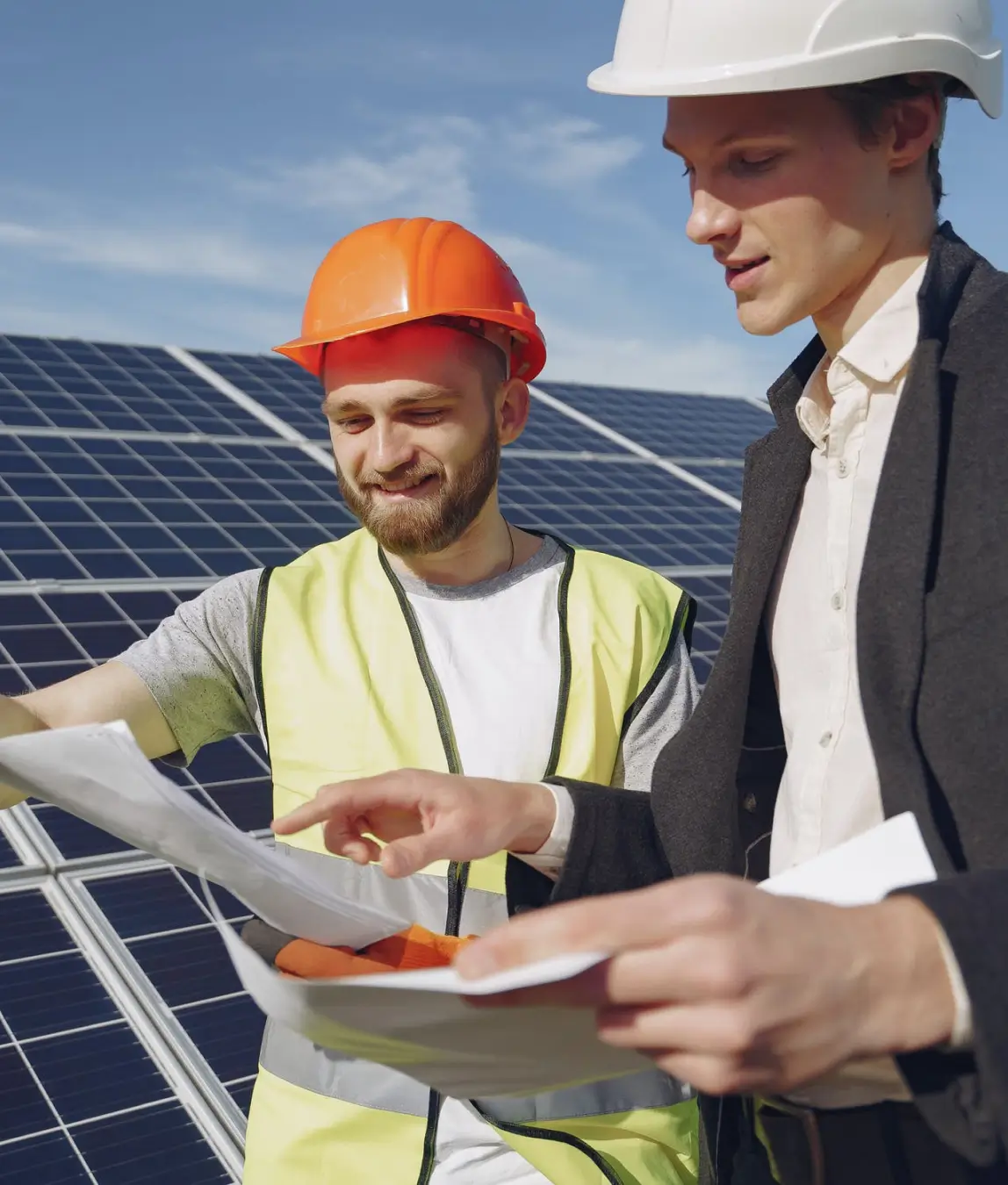 Engineers in hard hats looking at documents in front of solar panels