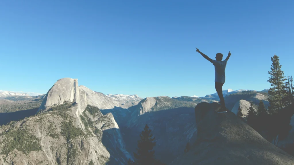 excited person at the end of a hike raising hands in accomplishment