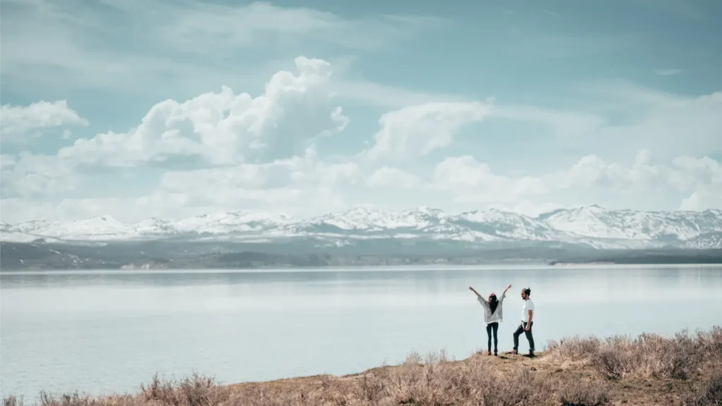 Couple standing on a lakeside overlook facing a mountain landscape, symbolizing long-term planning, future goals, and financial freedom.