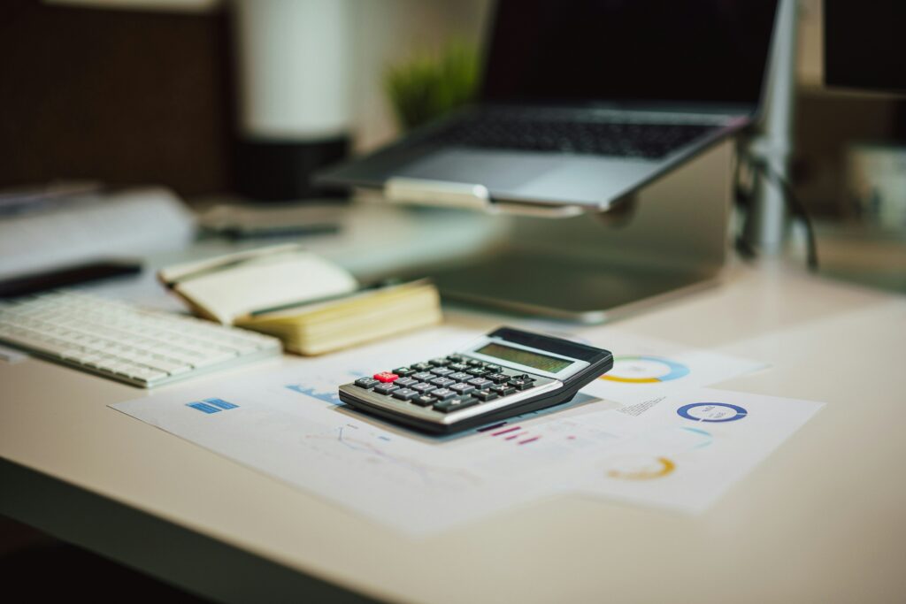 Abstract image of a computer open with a calculator and some random document with graphs on them referencing the blog post about the importance of a mid-year financial check-in.